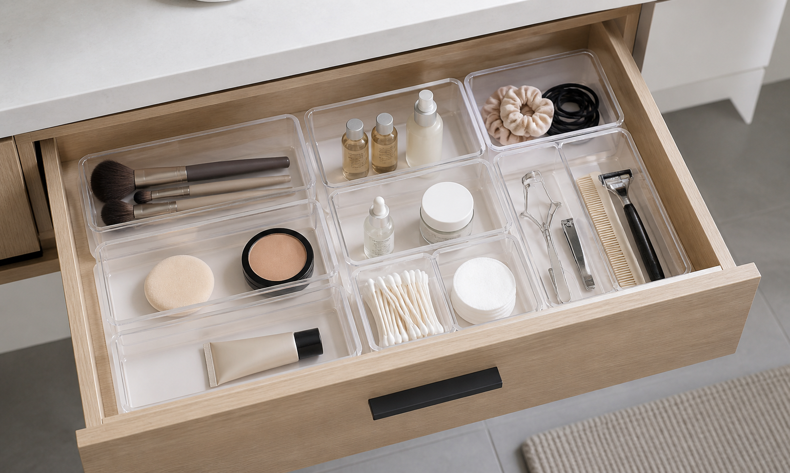 Clear modular organizer trays holding brushes, small bottles, cotton swabs, hair ties, and grooming tools inside an open bathroom vanity drawer